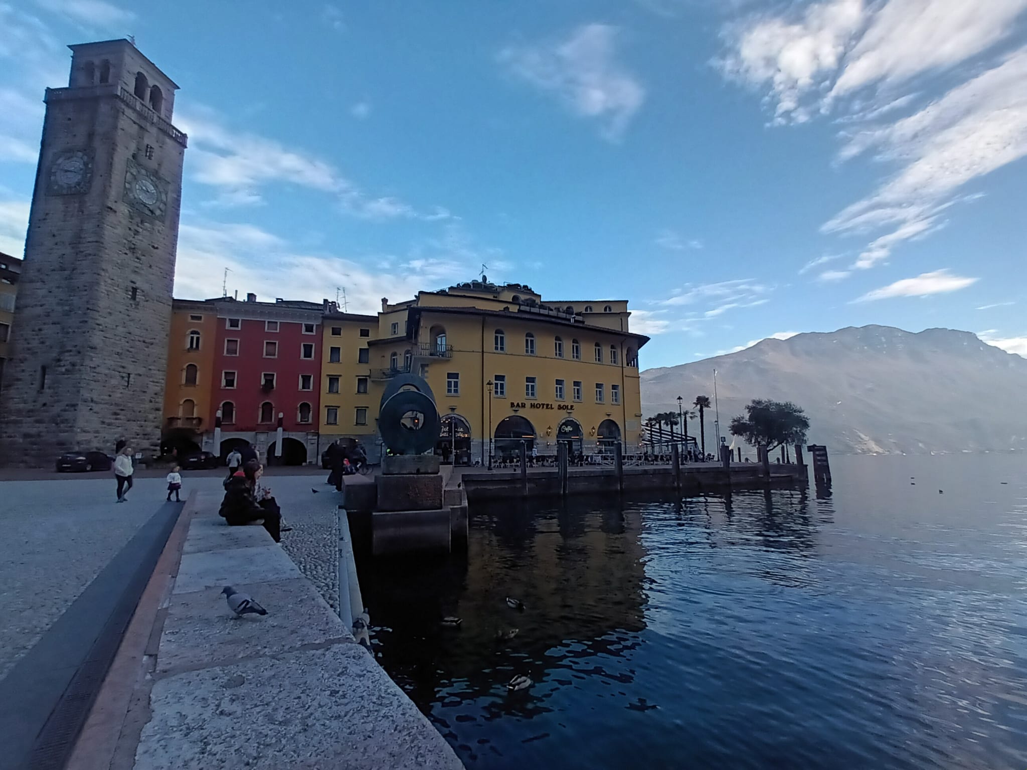 The tower beside the waterfront, with Bar Hotel Sole and a bronze ring sculpture on the quay